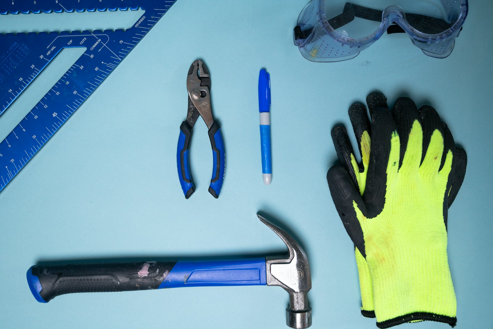 Measuring square, pliers, hammer, safety glasses, and gloves laid out for testing