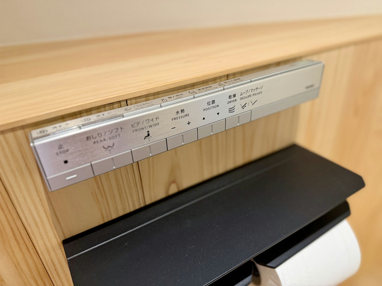 Close-up of a bidet attachment's side control panel showing pressure and position buttons